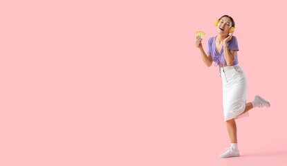Happy Asian woman with credit cards listening to music on pink background with space for text
