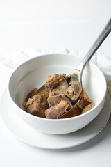 Overhead view of Nigerian goat pepper soup in a white soup plate, top view of goat meat pepper soup in a plate, traditional goat peppersoup in a white bowl