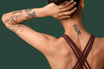 Tattooed young woman on green background, back view