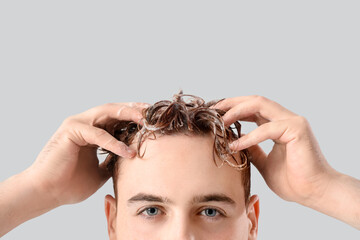 Young man washing hair against light background