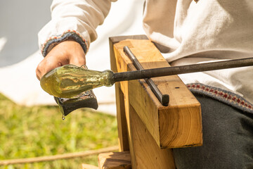 Glassblower or glassworker sculpting a section of the molten glass with old work tools and blowpipe...