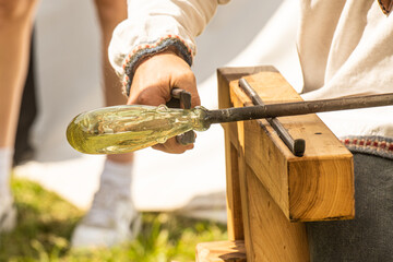 Glassblower or glassworker sculpting a section of the molten glass with old work tools and blowpipe...