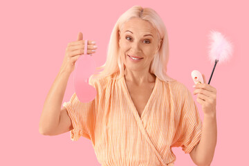 Mature woman with mask, vibrator and feather stick on pink background