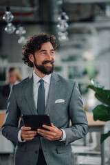 Fototapeta premium Smiling businessman holding tablet and looking away in modern office