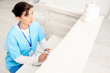 Female medical intern with clipboard working at reception in clinic