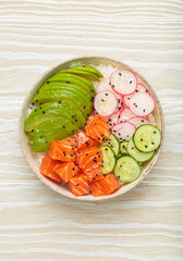 Poke bowl, a traditional hawaiian dish with diced raw salmon, avocado, vegetables served with rice and vegetables, a healthy meal on white wooden background