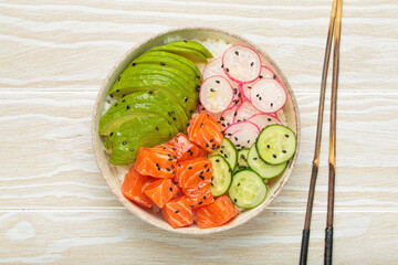 Poke bowl, a traditional hawaiian dish with diced raw salmon, avocado, vegetables served with rice and vegetables, a healthy meal on white wooden background