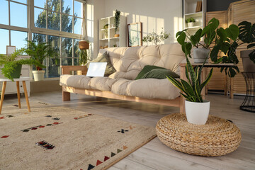 Interior of light living room with green plants and laptop on sofa