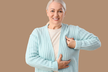 Mature woman checking her breast on brown background. Cancer awareness concept