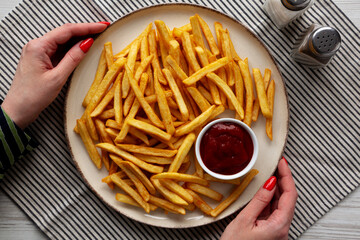 Female hands hold a plate with homemade Golden French Fries with Ketchup, top view.