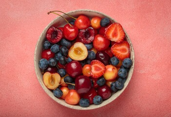 Simple, healthy, and delicious mix of fresh summer fruits is presented in a bowl, sitting on a textured pink background top view