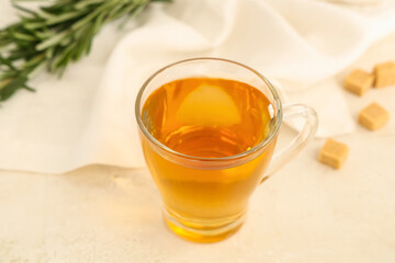 Glass cup of hot rosemary tea and sugar on beige background
