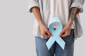 Young man with blue ribbon on light background, closeup. Prostate cancer awareness concept