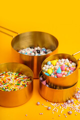 Measuring cups with sweet colorful sprinkles on orange background