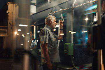 Senior man holding handrail on public transport at night