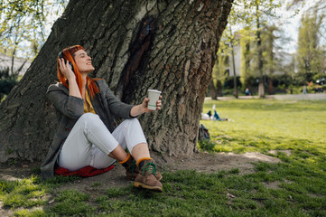 Young creative freelancer relaxing in park listening music and drinking coffee