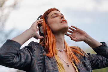 Young redhead businesswoman enjoying music with headphones in a park