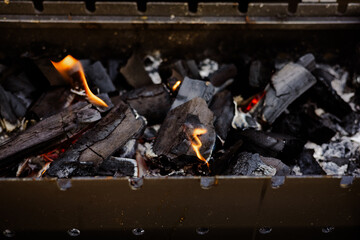 Burning charcoal with flames, ready for grilling season and cookouts. Close-up of burning charcoal in a grill, showcasing glowing embers and flames, perfect for summer barbecues and outdoor cooking.