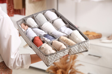 Beautiful young woman with clean clothes in organizer at wardrobe, closeup