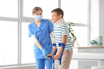 Injured little boy with crutches and doctor in clinic