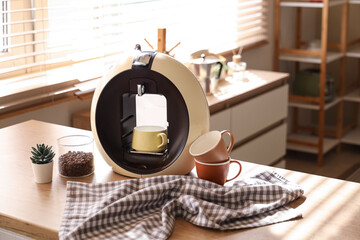Modern coffee machine with cups and jar of beans on table in kitchen