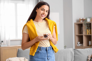 Pretty young woman with cup of hot coffee at home
