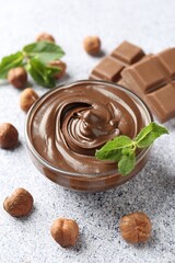 Tasty chocolate spread with mint in bowl and hazelnuts on grey textured table, closeup