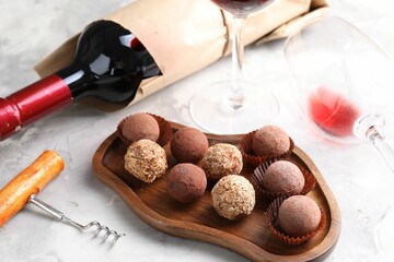 Delicious truffle bonbons and red wine on light grey background, closeup