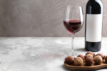 Delicious truffle bonbons and red wine on light grey background. Space for text