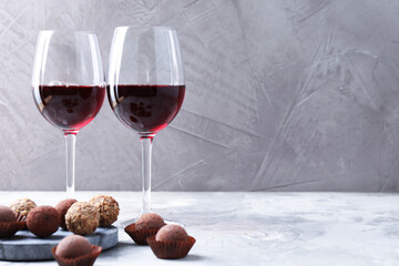 Delicious truffle bonbons and red wine on light grey background. Space for text