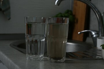 Glasses with clean and dirty water near sink indoors