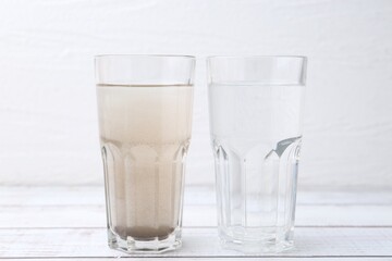 Glasses with clean and dirty water on white wooden table
