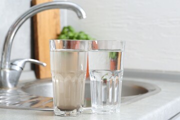 Glasses with clean and dirty water near sink indoors © New Africa