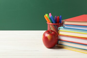 Different school stationery and red apple on white wooden table against blackboard, space for text