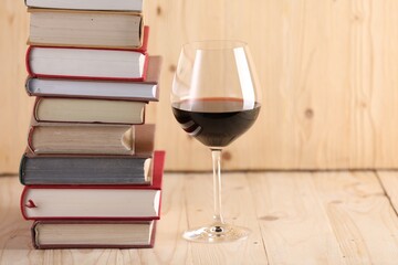 Glass of red wine and stacked books on wooden table