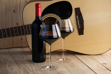 Acoustic guitar, bottle and glasses of red wine on wooden table