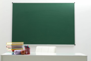 Different school stationery and apple on white table near blackboard indoors