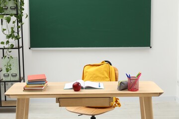 Different school stationery and red apple on wooden table near blackboard indoors