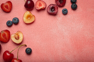 Vibrant arrangement of fresh fruit including strawberries, cherries, blueberries, and bananas on a textured pink surface with copy space