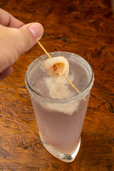 Close-up of a Chilled Lychee Cocktail in a Salt-Rimmed Highball Glass with Whole Lychee Garnish on a Rustic Wooden Surface