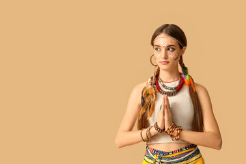 Beautiful young woman in Indian costume praying on beige background. Native American Heritage Month