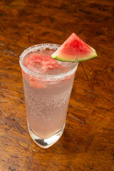 Close-up of a Refreshing Watermelon Cocktail with Salted Rim and Fresh Watermelon Slice Garnish on a Textured Wooden Table