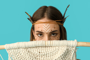 Beautiful young woman in Indian costume with macrame tapestry on blue background. Native American...
