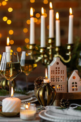 Beautiful table setting for family Christmas dinner at home. Cozy atmosphere, candlelight. Wine glasses, vintage chandelier, elegant interior. Fir tree branches, wooden furniture, dark, bokeh