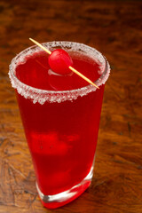 A classic red cherry cocktail with a sugar rim and maraschino garnish, a refreshing alcoholic beverage for a summer party at a bar, served in a glass on a wooden table.