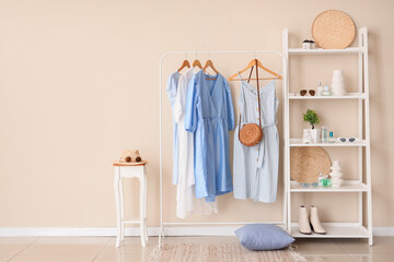 Rack with different stylish clothes and shelving unit with accessories near beige wall