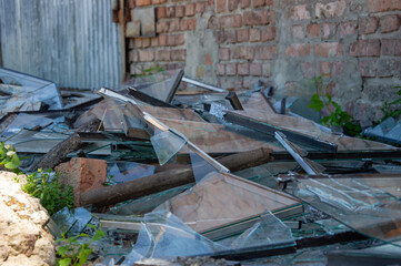 Shards of broken glass and wooden pieces lie on the ground beside a weathered brick wall,...