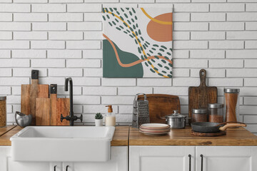 Table with sink and utensils near white brick wall in kitchen