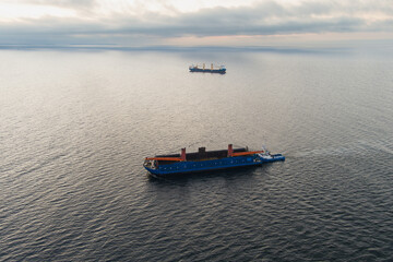 Aerial view of a tugboat pushing a large non-self-propelled barge with cargo on a calm sea. Concept of maritime logistics, shipping, and transportation.