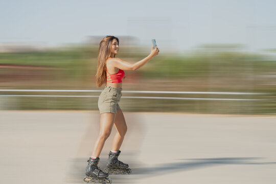 Young woman roller skating and taking a selfie with her smartphone in a park, enjoying a sunny day - Powered by Adobe